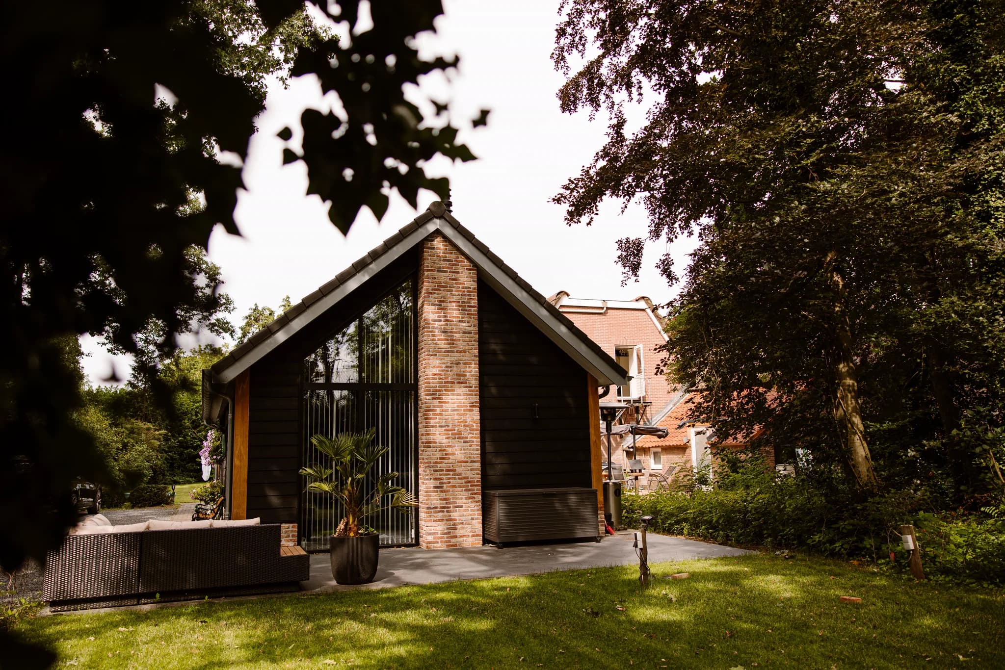 Moderne houten schuur met grote ramen en bakstenen schoorsteen gelegen in een tuin met groen gras en bomen