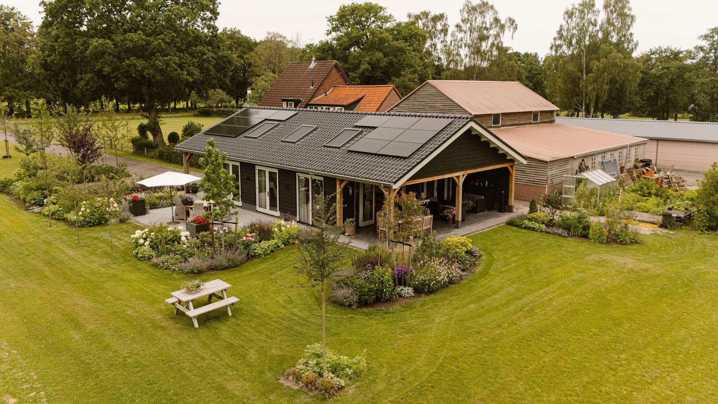 Moderne woning met zonnepanelen op dak en groene tuin met bloemen en bomen