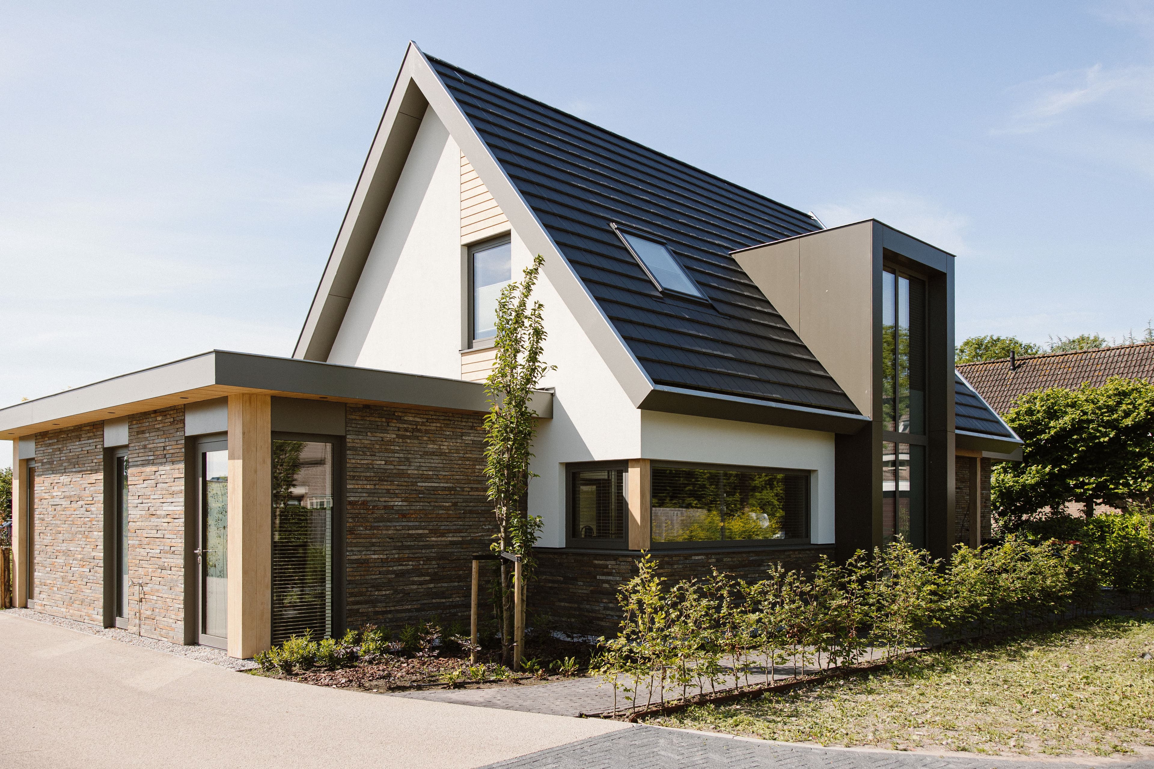 Voorgevel van een moderne woning met zwart puntdak, dakraam, steenstripgevel en grote ramen